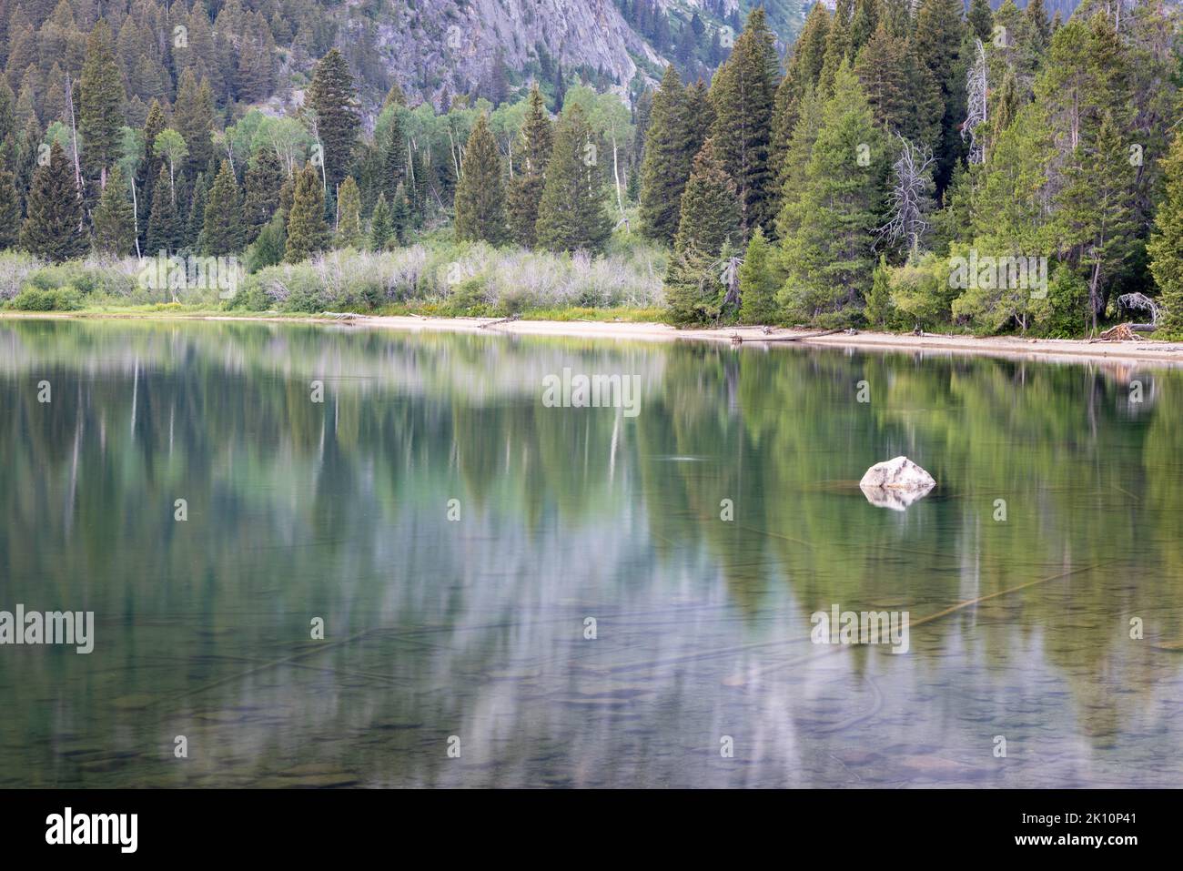 A Lone Rock Protruding From The Surface Of The Waters Reflecting The A Lone Rock Protruding From The Surface Of The Waters Reflecting The